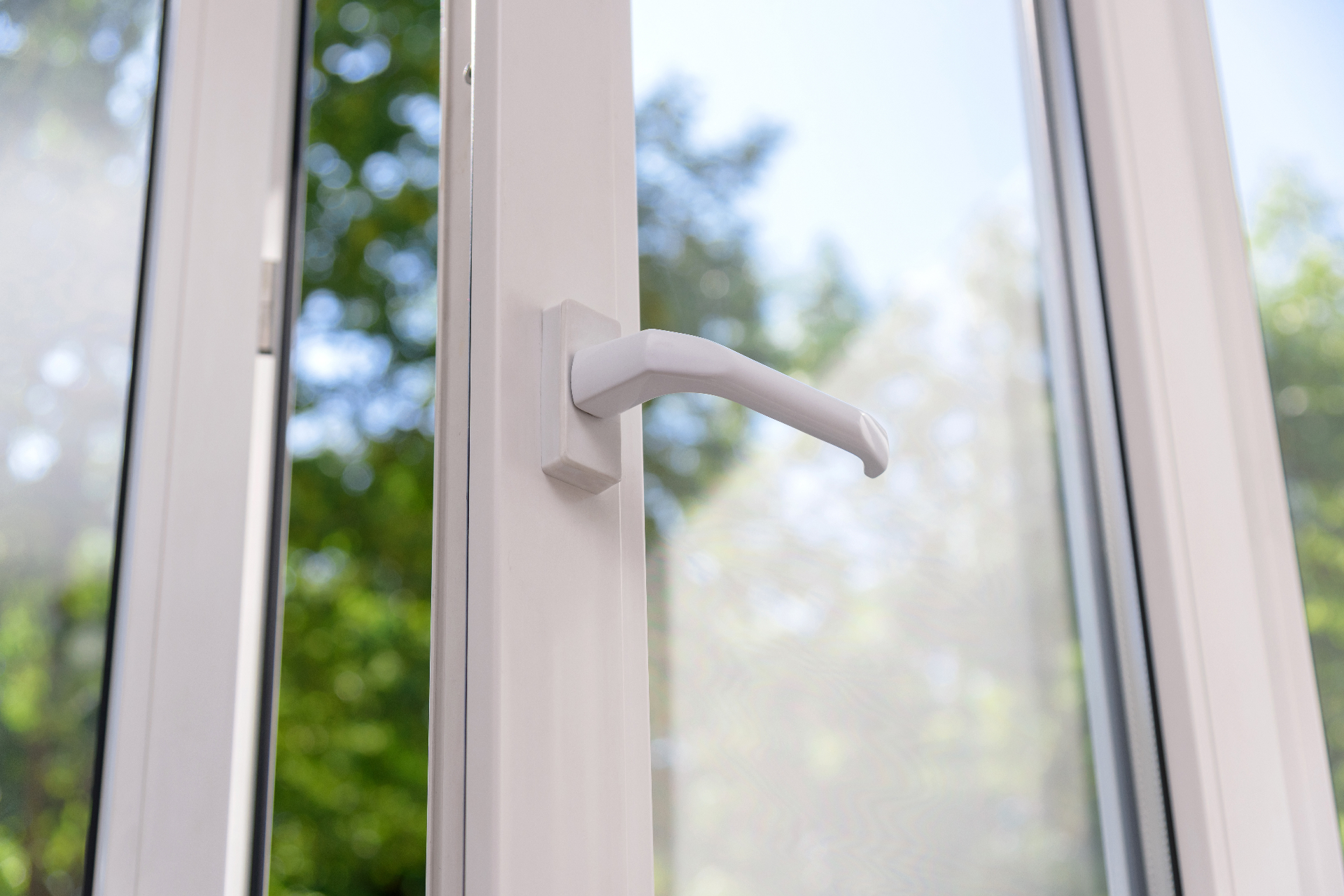 Detailaufnahme eines weißen Fenstergriffs mit Blick ins Grüne